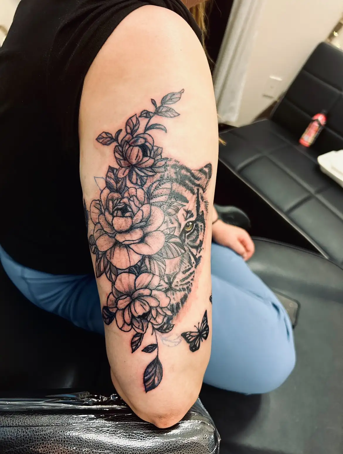 BL-ink Tattoo Colorado Springs outer-arm piece: black-grey peonies framing a realistic tiger face, finished with a small butterfly at the elbow.